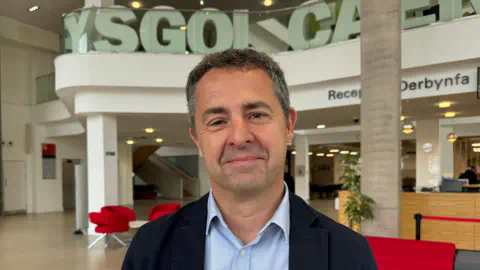 Professor of endocrinology Aled Rees smiling into the camera at Cardiff University. He is wearing a blue jacket and a blue shirt.