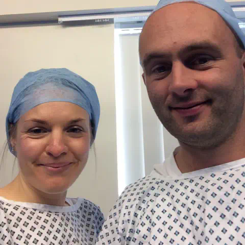 Family photo Annika and husband Eulyn smiling at the camera, and wearing medical clothing, during IVF treatment before their son was born in 2018